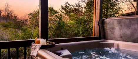 A hot tub with a control panel, a towel, and a drink on a tray, overlooking a natural landscape.