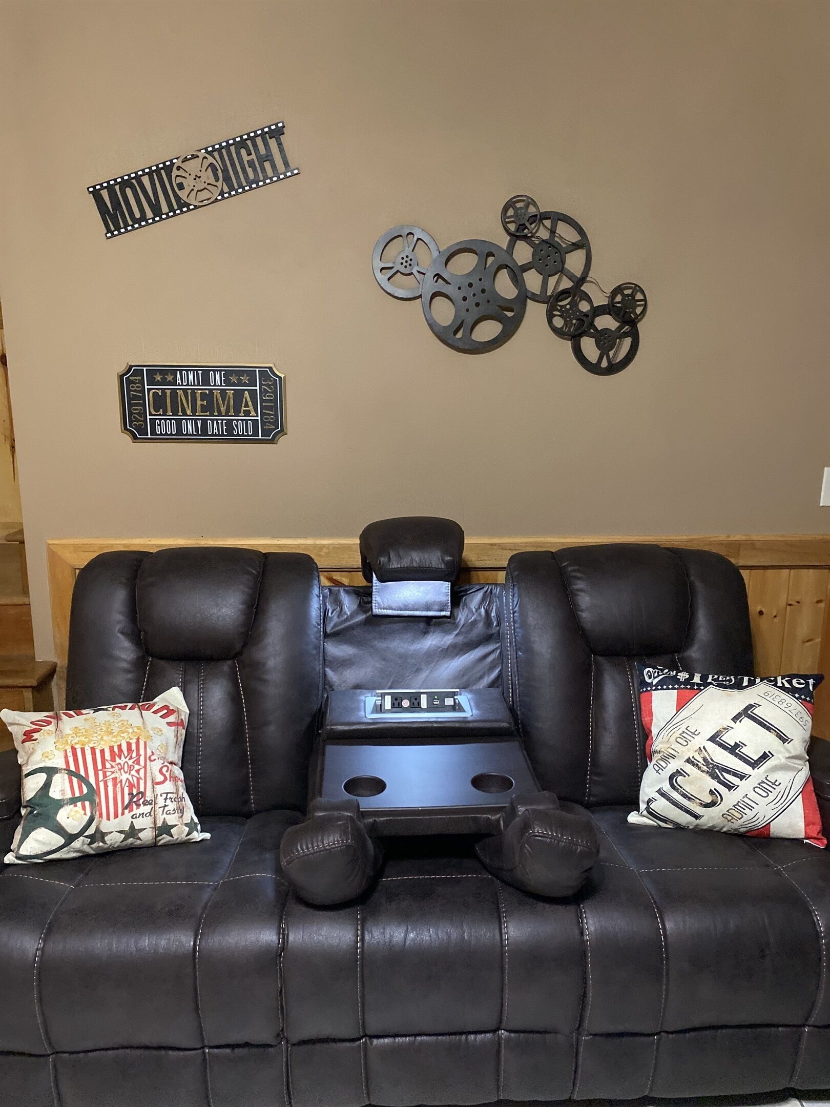 A black leather recliner with a built-in massage chair, a small table, and a pillow with a cinema ticket design.