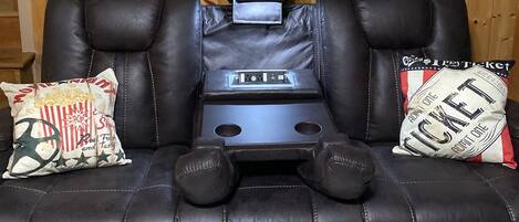 A black leather recliner with a built-in massage chair, a small table, and a pillow with a cinema ticket design.