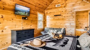 A cozy wooden cabin room with a bed, a TV mounted on the wall, and a sign reading "Bear Country". - Pet Friendly Cabin|Hot Tub|Pool Table|Outdoor Fireplace (Blue Ridge)
