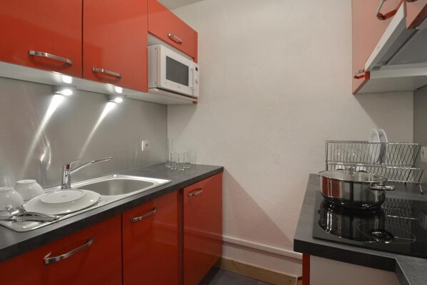 Compact kitchen with modern design, featuring a stainless steel sink, microwave oven, and black stovetop.