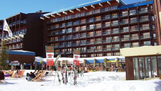 Un hotel de varios pisos con balcones, esquíes y zonas de estar al aire libre.