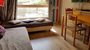 Un dormitorio con cama, escritorio y silla. Se ve un paisaje montañoso por la ventana.