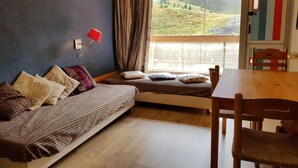 Una habitación acogedora con sofá cama, una mesa de comedor de madera y vistas a un paisaje montañoso a través de un ventanal grande.