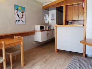 Kompakti keittiö, jossa on mikroaaltouuni, kahvinkeitin ja puiset kaapit.