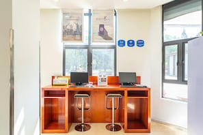 A reception desk with two computers, a printer, and a QR code dispenser. There are two bar stools, a window with a view of trees, and a 'No Smoking' sign. - Hanting Hotel (Shanghai)