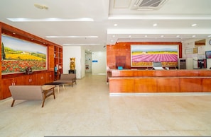 A reception area with a wooden reception desk, a large painting of a field, and a statue. - Hanting Hotel (Shanghai)