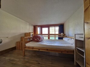 A single wooden bed with a mattress and pillows in a room with a sloped ceiling and a window. - 300m from ski slopes, 5th floor, balcony, tv, 33m², Les Arcs (Les Arcs)