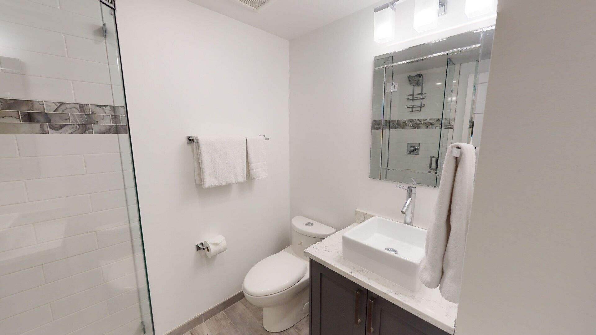 A modern bathroom with a glass shower enclosure, a toilet, a sink, and a mirror.