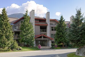 A multi-story building with stone pillars, a red roof, and a landscaped front yard with trees and shrubs. - Greyhawk by Whistler Premier (Whistler)