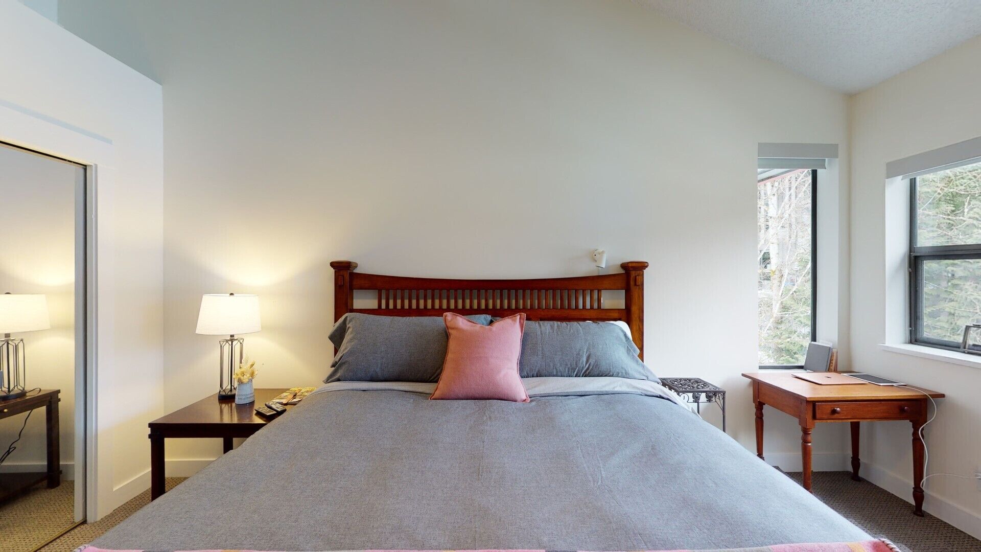 Une chambre à coucher bien rangée, avec un lit, des tables de chevet, une lampe et une vue sur les arbres par la fenêtre.