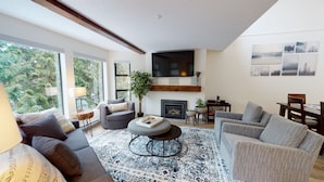 A modern living room with a fireplace, large windows, and a flat-screen TV. - Greyhawk by Whistler Premier (Whistler)