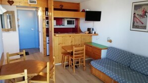 A compact room with a kitchenette, a wooden dining table with chairs, a sofa, and a television mounted on the wall. - 50m from shops, 3rd floor, view resort, balcony, tv, 33m², Les Arcs (Les Arcs)