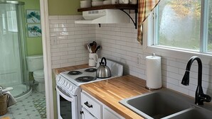 A kitchen with white cabinets, a wooden countertop, a stove, a sink, and a window with a plaid curtain. - Hilltop Cottage steps from East Coast Trail, fishing & whale watching (Cape Broyle)