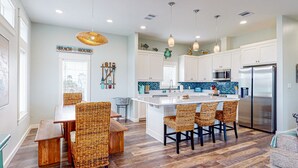 A modern kitchen with white cabinets, a central island with bar stools, a stainless steel refrigerator, and a backsplash with blue tiles. - Heated Private Pool, Yard Games, Golf Cart Included (Port Aransas)