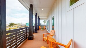 A covered outdoor area with wooden flooring, orange chairs, and a wooden railing. - Heated Private Pool, Yard Games, Golf Cart Included (Port Aransas)