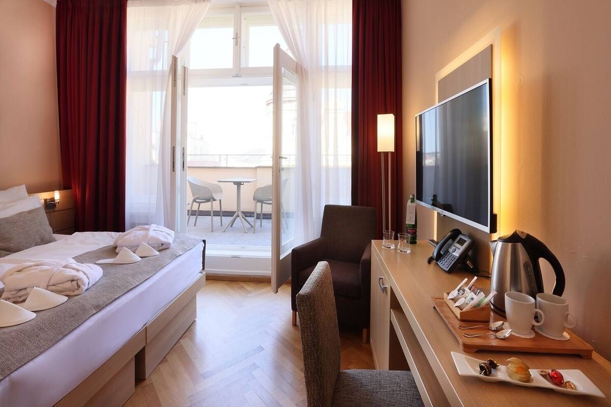 Una habitación de hotel con cama, escritorio con teléfono, televisor y balcón con sillas.