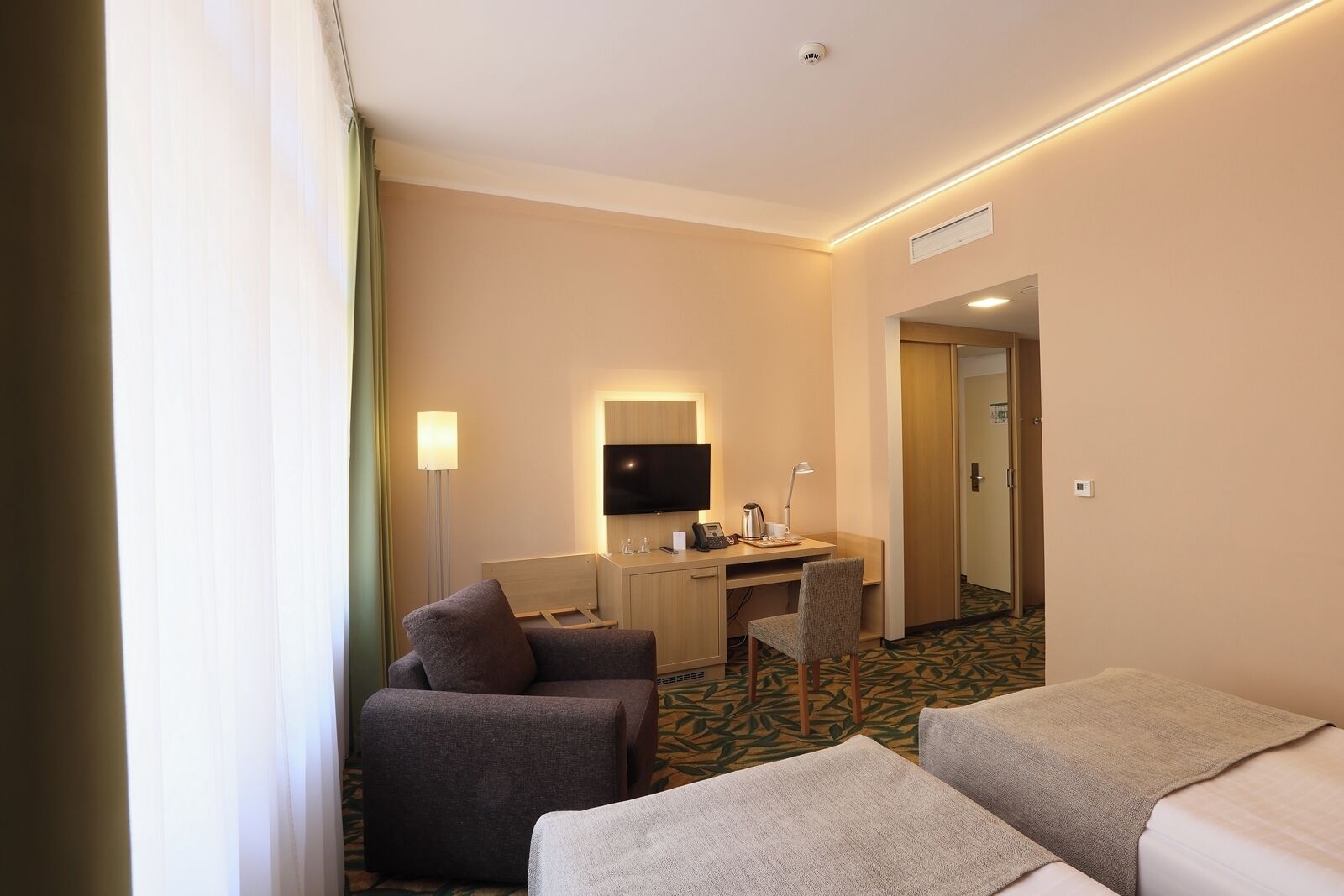 A hotel room with a desk, two chairs, a television, and a bed.