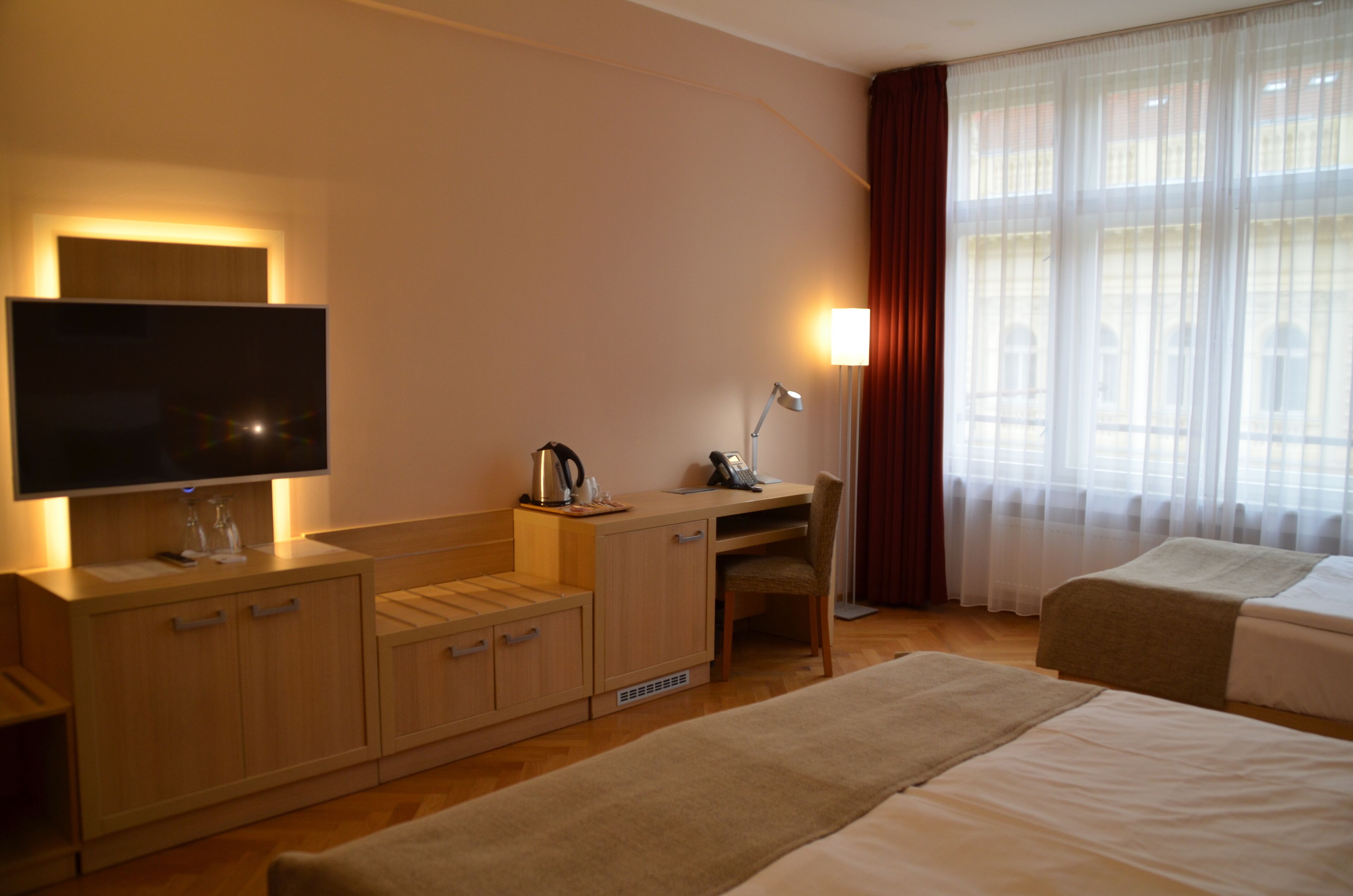 Une chambre d’hôtel équipée d’une télévision, d’un bureau, d’une chaise, de deux lits et d’une fenêtre avec des rideaux.