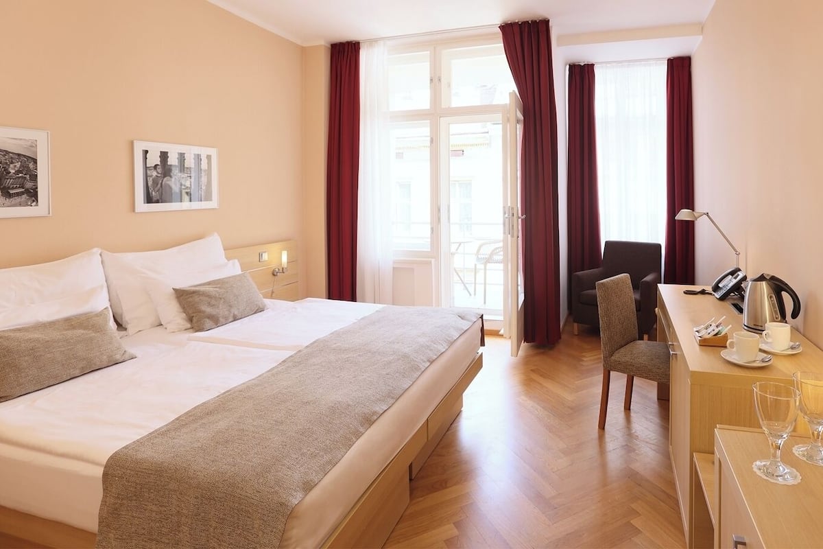 Una habitación de hotel con una cama grande, un escritorio con silla, televisión y ventana con cortinas.