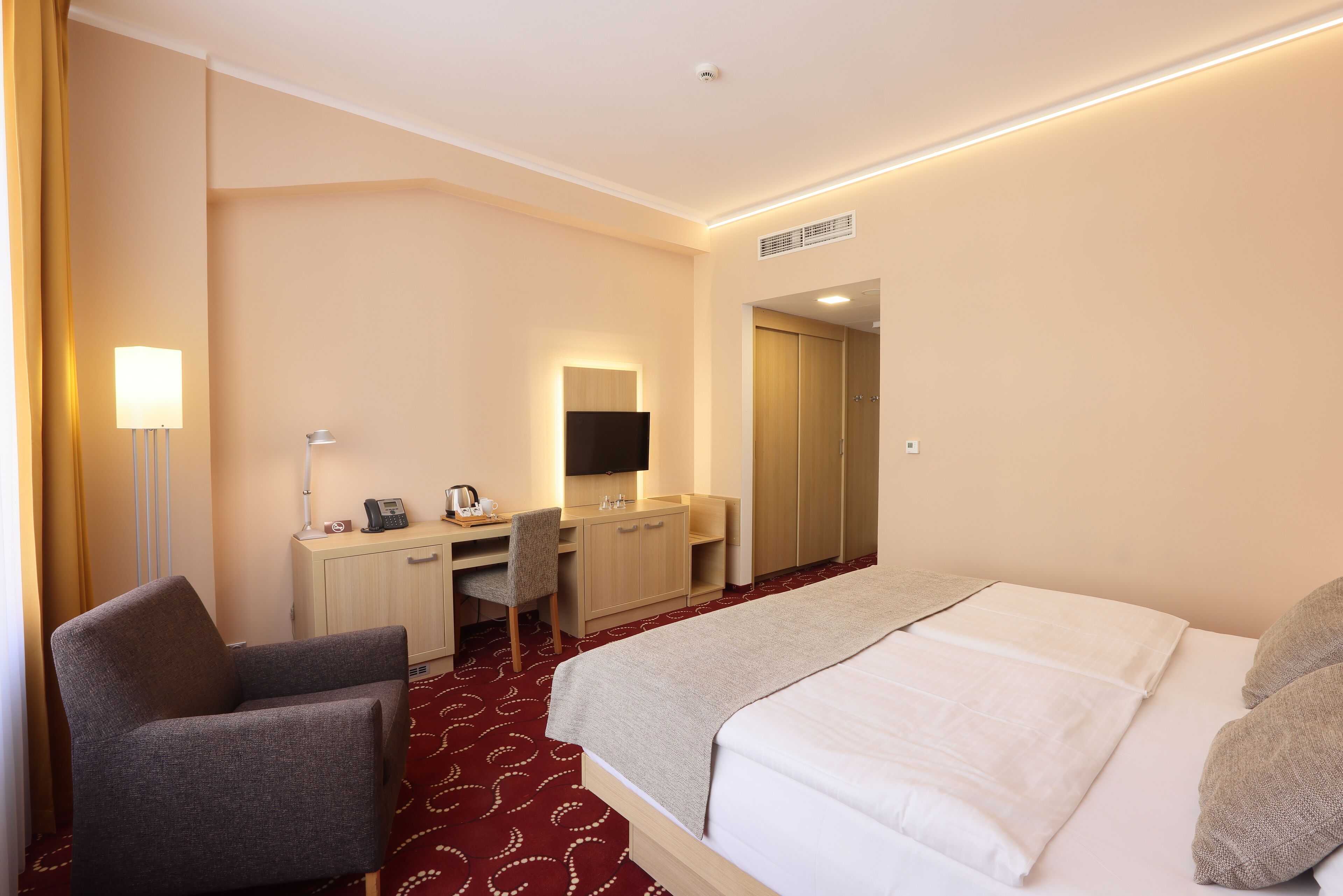 A hotel room with a bed, a desk with a chair, a TV, and a wardrobe.