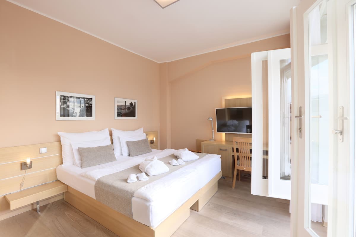 Una habitación de hotel moderna con una cama grande, mesitas de noche, un escritorio con silla y un televisor.