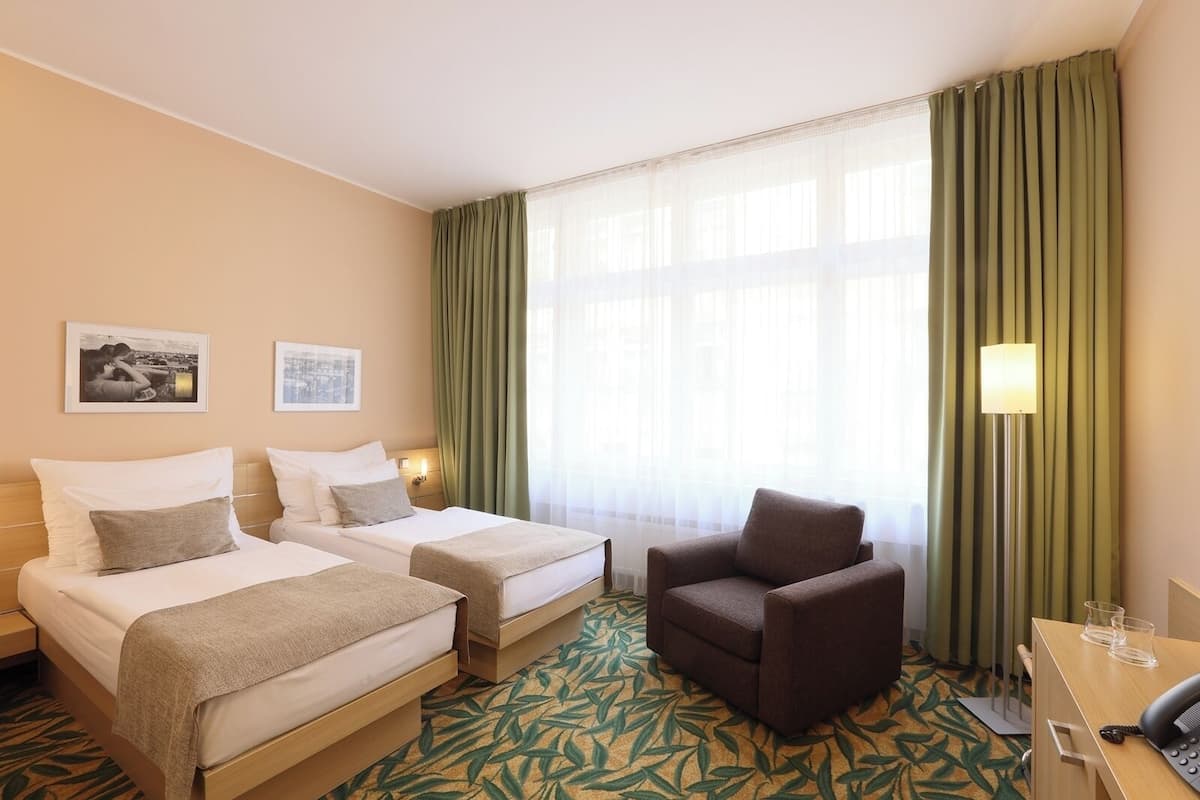 Habitación de hotel con dos camas, una silla, un escritorio con teléfono y una ventana con cortinas.