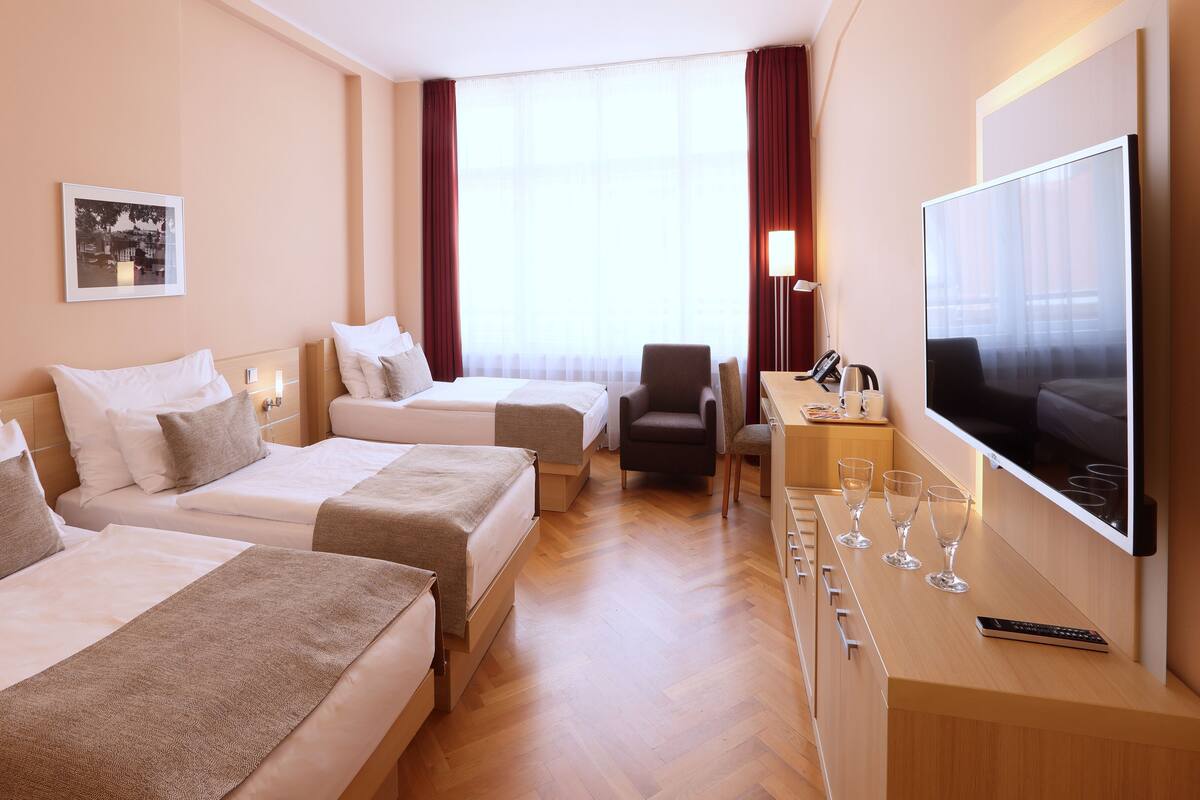 Una habitación de hotel con dos camas, un escritorio con televisor y una silla.