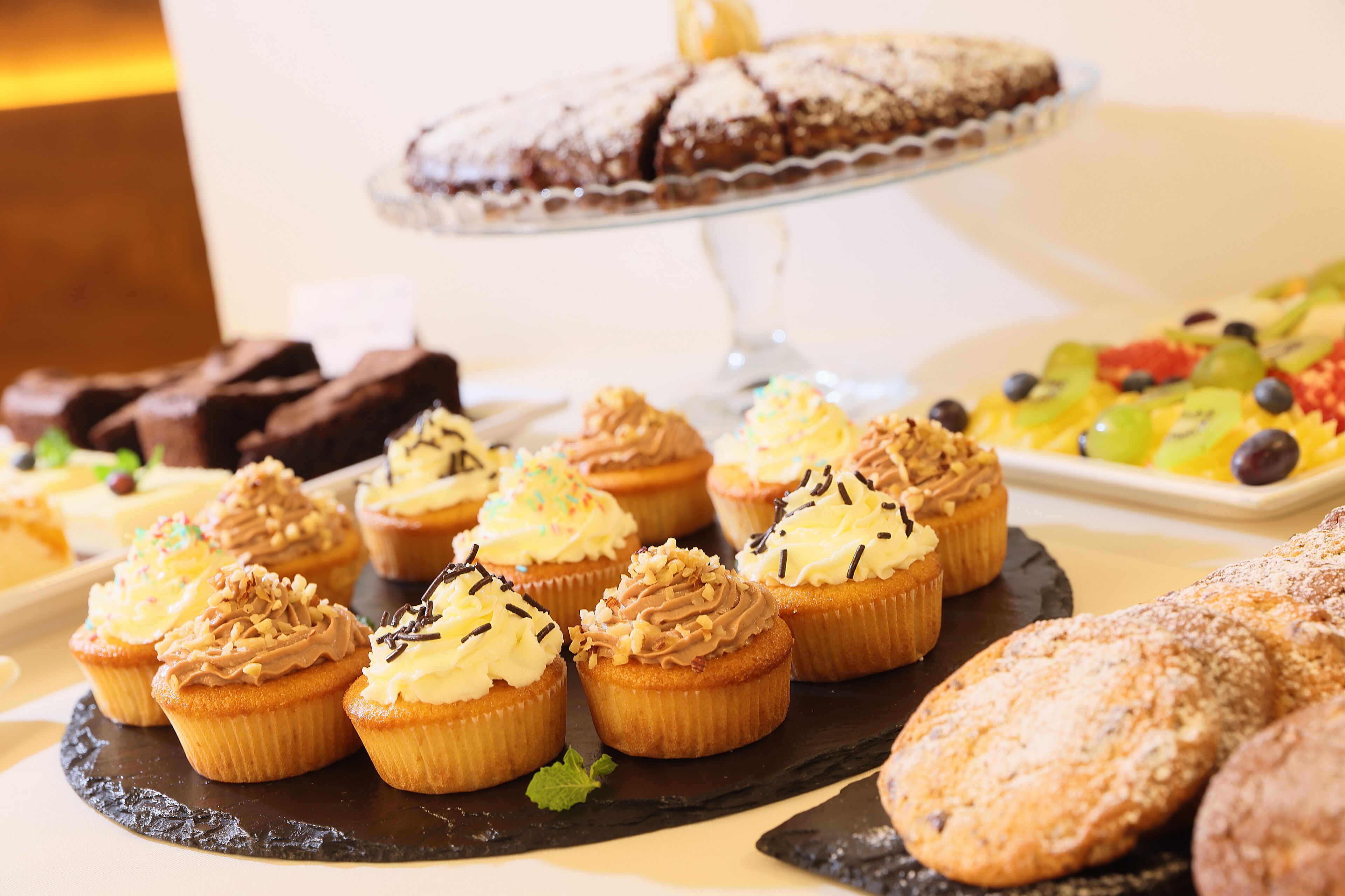 A variety of desserts on a buffet table, including cupcakes, brownies, and a cake on a stand.