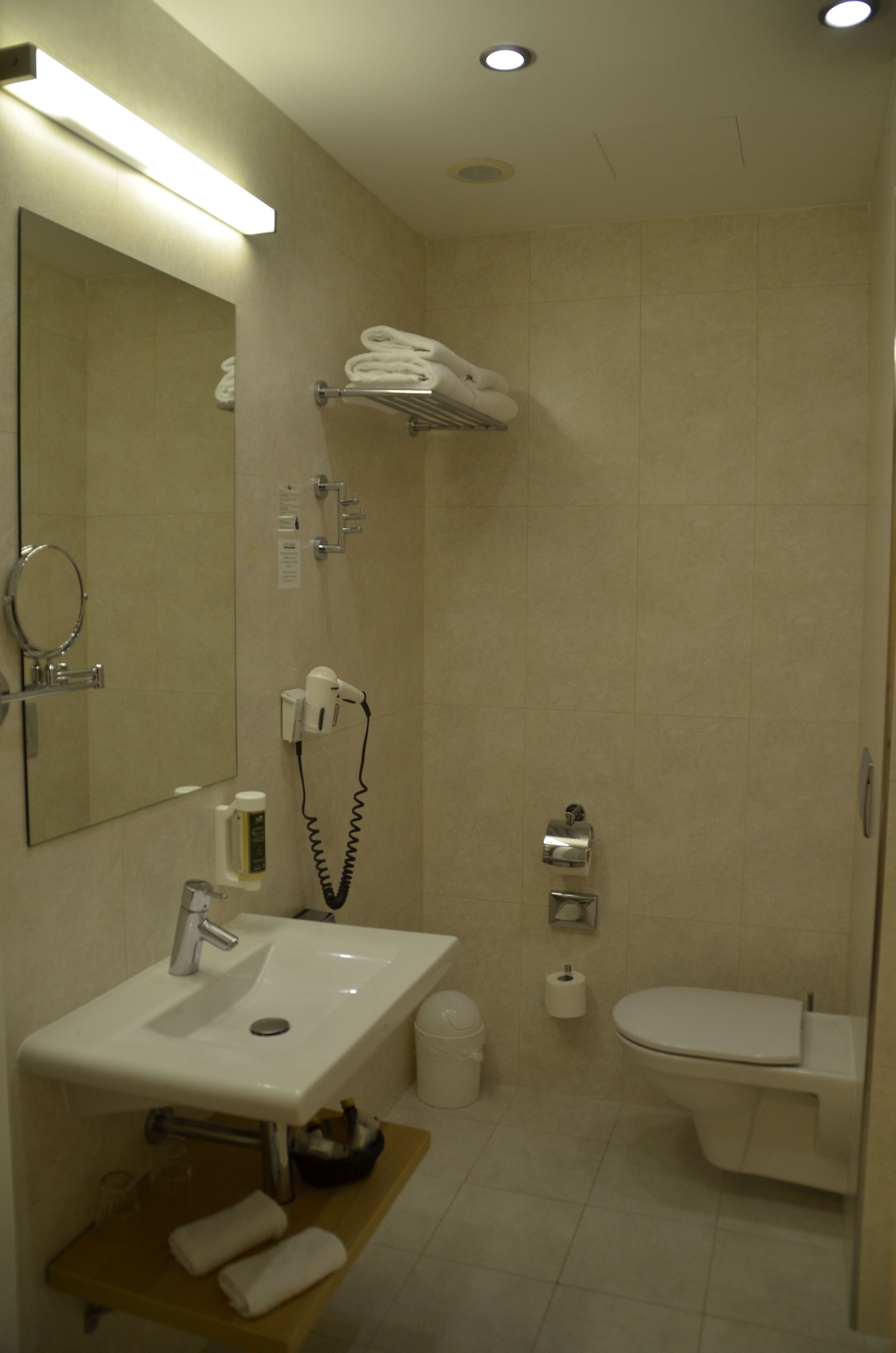 Ein modernes Badezimmer mit Waschbecken, Spiegel, Handtuchhalter, Dusche, Toilette und einer kleinen Ablage für Pflegeprodukte.