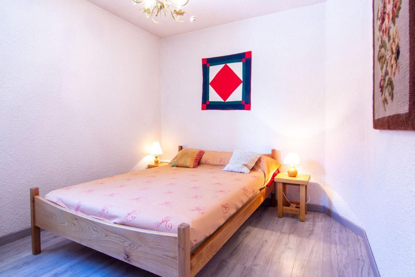 A bedroom with a wooden bed, two bedside tables with lamps, a floral-patterned bedspread, and a wall hanging.