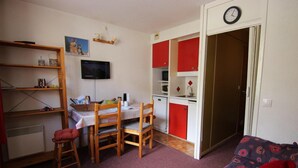Ett kompakt bostadsutrymme med ett matbord, stolar, en TV, ett litet kök och en soffa.