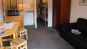 Ein gemütlicher Wohnraum mit Küchenzeile, einem Essbereich mit Holztisch und Stühlen sowie einem schwarzen Sofa.