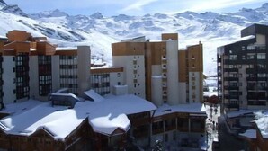 Ein mit Schnee bedeckter Gebäudekomplex mit mehreren Etagen und Balkonen, vor einer Kulisse schneebedeckter Berge.