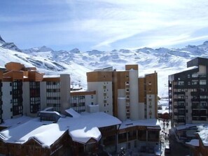 A snow-covered building complex with multiple floors and balconies, set against a backdrop of snow-capped mountains. - 100m from resort center, 4th floor, balcony, tv, 24m², Val Thorens (Val Thorens)