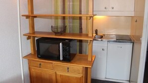 Eine kompakte Küche mit einer Mikrowelle auf einem Holzboden, einem kleinen Kühlschrank und einem Spülbecken.
