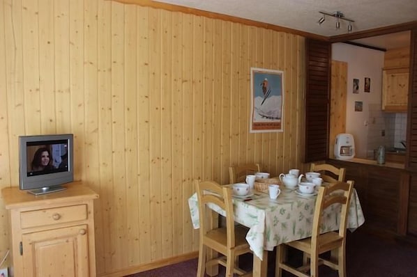 A dining area with a wooden wall, a television on a small cabinet, and a table set with cups and a teapot.