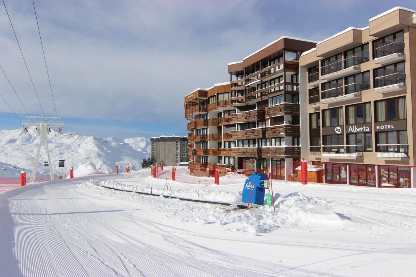 Un hôtel moderne doté de nombreux balcons, avec un télésiège visible au loin et un paysage enneigé.
