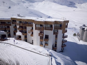 A multi-story hotel with balconies, set against a snowy mountain backdrop.