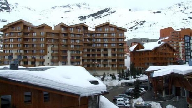 Un immeuble en bois à plusieurs étages, doté de balcons, entouré de montagnes enneigées.