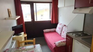 Une pièce compacte comprenant un coin cuisine, une petite table à manger, un canapé et une fenêtre avec des rideaux.