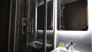 Une salle de bain moderne avec une douche à parois de verre, un lavabo blanc agrémenté d’articles de toilette et un grand miroir.