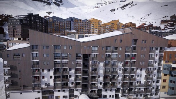 Un hotel de varios pisos con balcones y una montaña nevada al fondo.