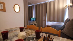 Una habitación de hotel con una cama, un escritorio con una computadora, una mesa con tazas y un objeto decorativo, y cortinas.