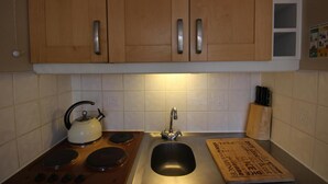 Una cocina con armarios de madera, estufa, pileta y tetera.