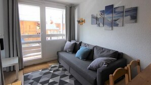 Una sala de estar con un sofá, una silla de madera, un tapete estampado y un ventanal corredizo que da a un área exterior.
