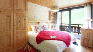 Ein Schlafzimmer einer Holzhütte mit einem großen Bett, einem Holzschrank und einem Balkon mit Blick.