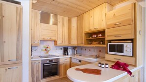 Eine kompakte Küche mit Holzausstattung, einer Mikrowelle, einer Kaffeemaschine und einem Schneidebrett auf der Arbeitsfläche.