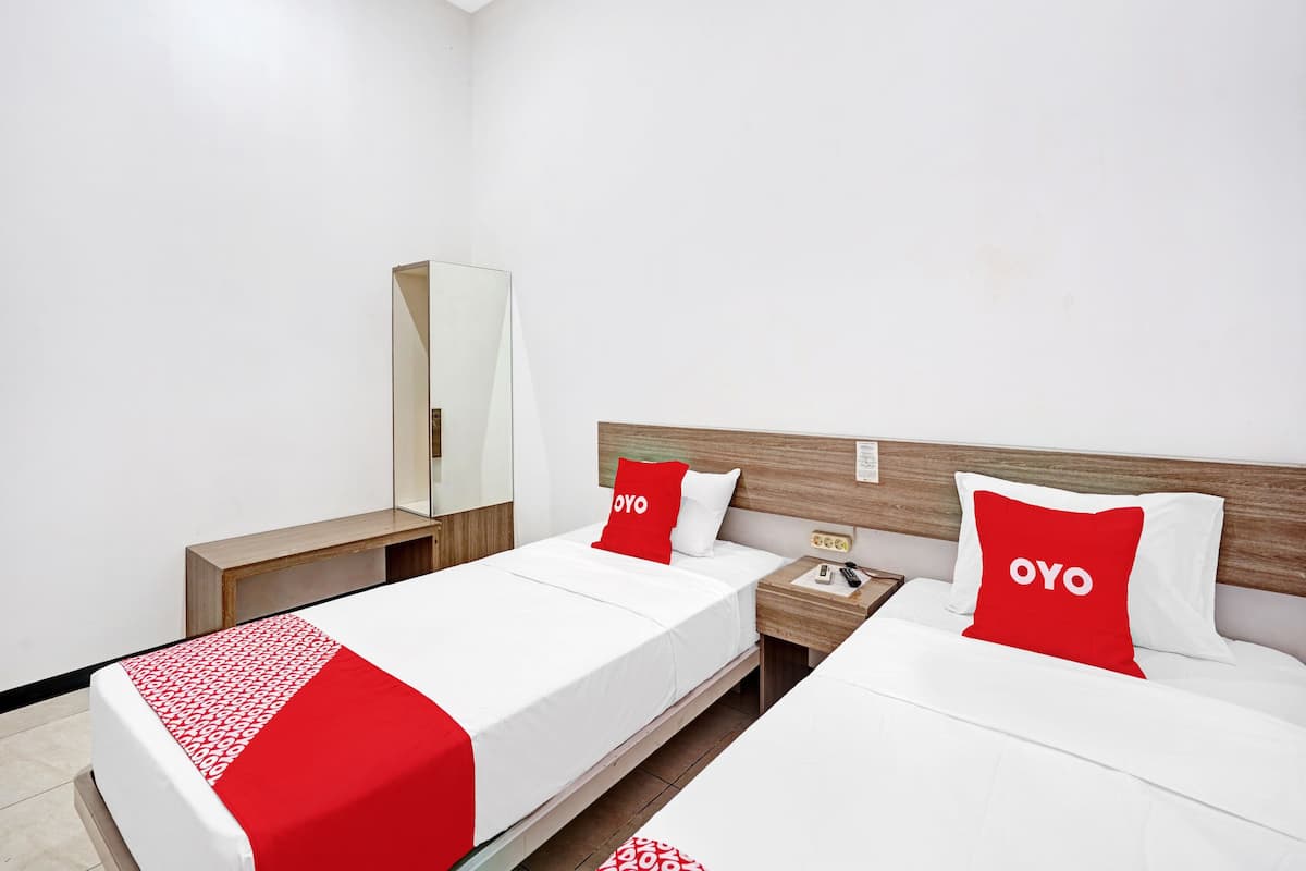 Habitación de hotel con dos camas, cabecera de madera, mesita de noche, espejo y colcha roja y blanca.