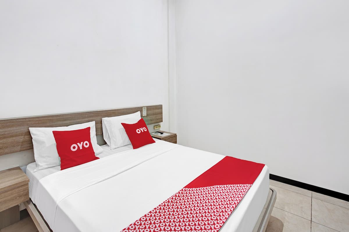 Una cama bien hecha con ropa blanca y almohadas rojas, cabecera de madera y un plaid rojo y blanco.